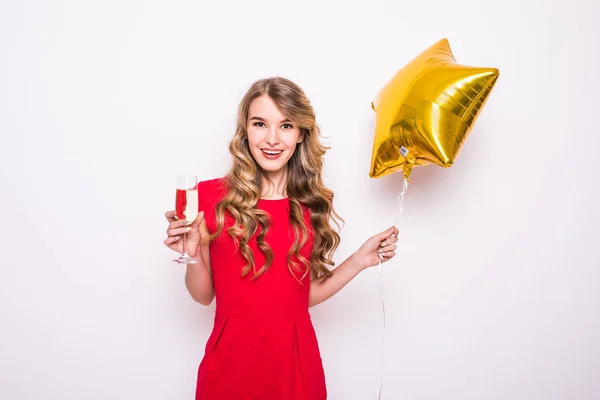 Mujer joven en vestido rojo con globo en forma de estrella de oro sonriendo y bebiendo champán sobre fondo blanco —  Fotos de Stock