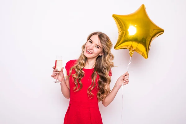 Mujer joven en vestido rojo con globo en forma de estrella de oro sonriendo y bebiendo champán sobre fondo blanco — Foto de Stock