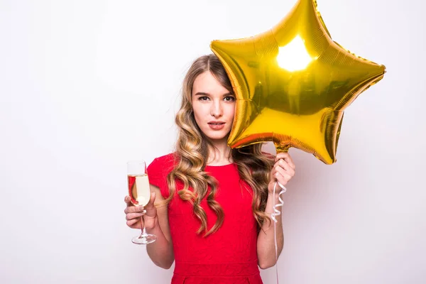 Mujer joven en vestido rojo con globo en forma de estrella de oro sonriendo y bebiendo champán sobre fondo blanco — Foto de Stock