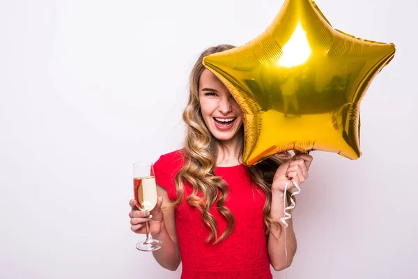 Fiatal nő, piros ruhás, arany csillag alakú léggömb mosolyogva, és ivott pezsgőt felett fehér háttér — Stock Fotó