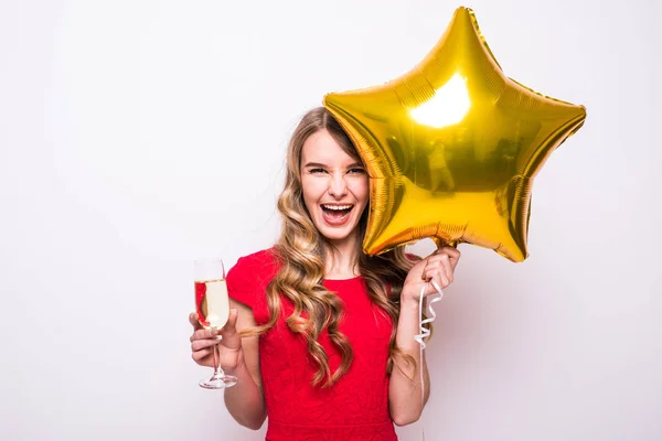 Mujer joven en vestido rojo con globo en forma de estrella de oro sonriendo y bebiendo champán sobre fondo blanco —  Fotos de Stock