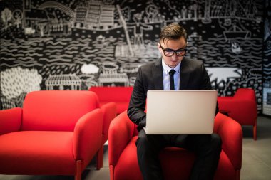 gözlük modern ofiste otururken dizüstü bilgisayarda çalışan genç adam