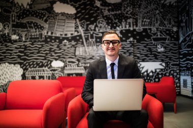 İşadamı ofiste otururken dizüstü bilgisayarda çalışma gözlük gülümsemek