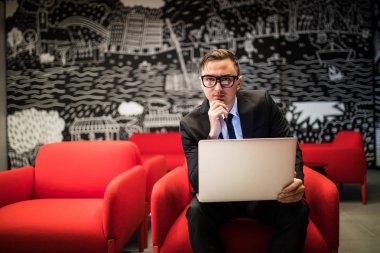 gözlük ofiste otururken dizüstü bilgisayarda çalışan genç işadamı