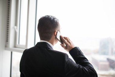 Onun üst kat ofis büyük pencereler yanında duran, cep telefonundan konuşurken kenti seyir yakışıklı genç iş adamı