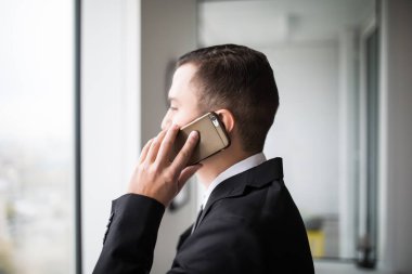 Onun üst kat ofis büyük pencereler yanında duran, cep telefonundan konuşurken kenti seyir yakışıklı genç iş adamı