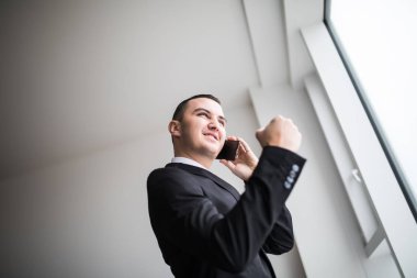 Onun üst kat ofis büyük pencereler yanında duran genç iş adamı kenti almak iyi haber ise onun bakarak konuşmak üstünde hareket eden telefon