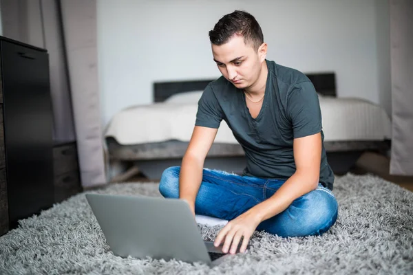 Hombre joven acostado en la alfombra mientras usa el ordenador portátil — Foto de Stock