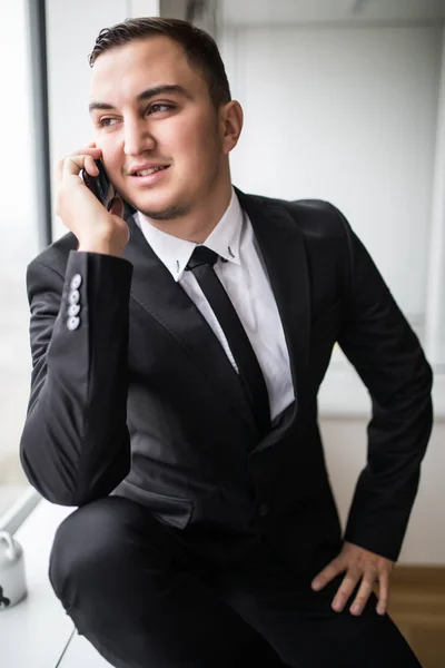 Pohledný mladý podnikatel v elegantní moderní kancelářské prostory s velkými okny, mluví o telefonu — Stock fotografie