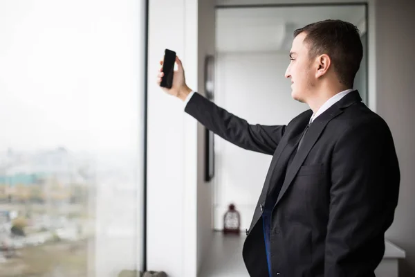 Stilig ung affärsman i en elegant moderna kontorslokaler med stora fönster, tar selfie i telefon — Stockfoto