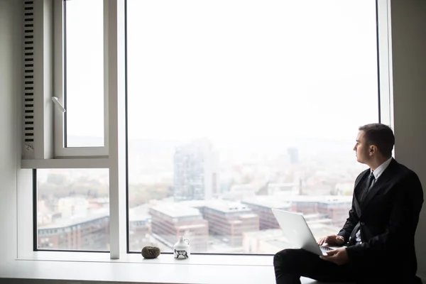 Jeune homme d'affaires travaillant près de la fenêtre panoramique de la ville sur ordinateur portable — Photo