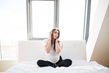Pencere arka plan, evde yatakta smartphone üzerinden müzik kulaklık ile genç kadın