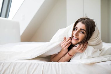 gülümseyen kadın yatak odasında bir yorganın altında