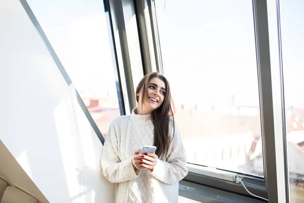 Girl text sms on phone at big window at home room — Stock Photo, Image