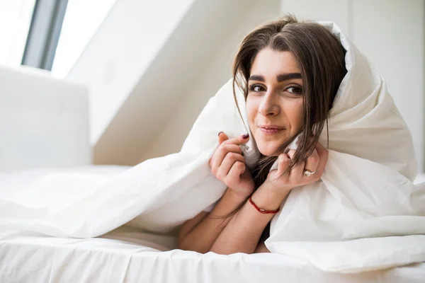 笑顔の女性彼女のベッドルームで羽布団の下 — ストック写真