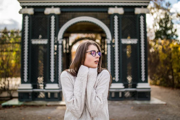 Девушка в свитере и в очках в осеннем саду замка — стоковое фото