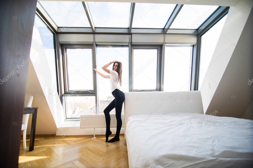 Woman standing near the window while stretching near bed