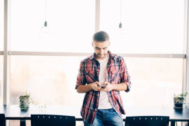 Genç adam yazmak içinde telefon vasıl büyük pencere ofiste.