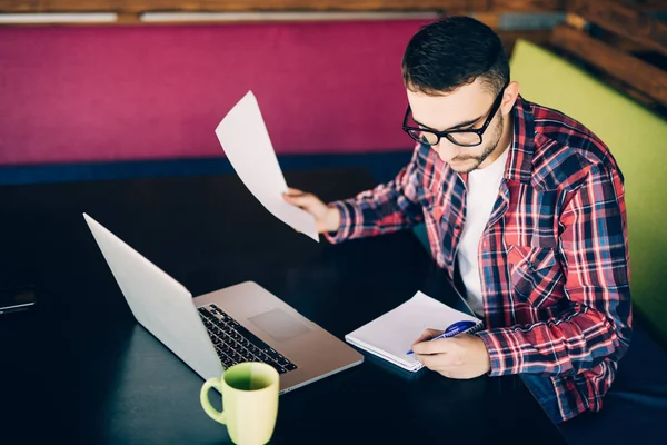 Belgeler ve dizüstü bilgisayar ile kanepede oturan ve bir şeyler yazıyor adam. Coworking