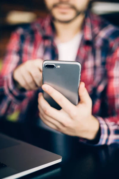 Close up van de man in rode shirt zittend op de Bank door de tabel met telefoon — Stockfoto