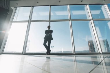 Pazar kralı. Genç başarı iş adamı ayakta karşılamak panoramik pencerelere karşı