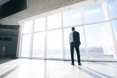 Genç işadamı ceket ile modern ofis panoramik pencerelere omuz üzerinden rahat