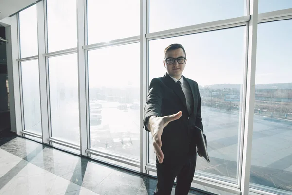 Pohledný podnikatel v obleku a brýle dát handshake v místnosti úřadu s panoramatickými okny — Stock fotografie