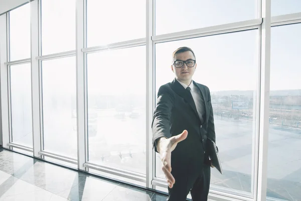 Bello uomo d'affari in giacca e cravatta e occhiali dare stretta di mano in ufficio con finestre panoramiche — Foto Stock