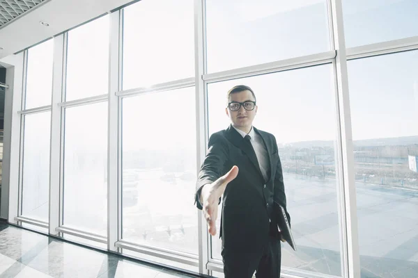 Красивий бізнесмен в костюмі і окулярах дає рукостискання в офісній кімнаті з панорамними вікнами — стокове фото