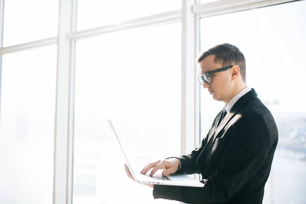 Beau homme d'affaires en costume et lunettes avec ordinateur portable contre fenêtre panoramique salle . — Photo