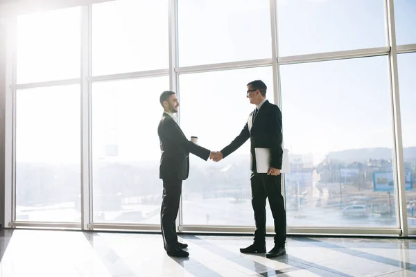 Два бізнесмени вітають з рукостисканням в офісі з панорамними вікнами — стокове фото