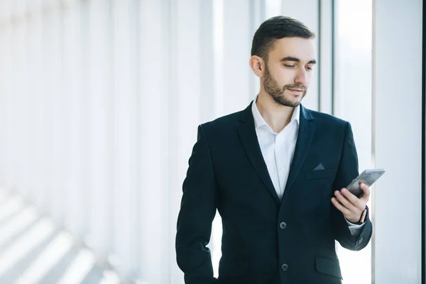 Przystojny biznesmen w garnitur spojrzenie na smartfonie w biurze — Zdjęcie stockowe