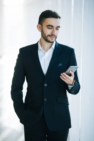 Красивий бізнесмен у костюмі дивиться на смартфон в офісі — стокове фото