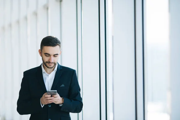 Pohledný podnikatel v obleku textu sms na telefonu v kanceláři — Stock fotografie