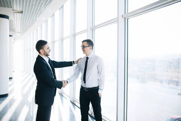 Dos hombres de negocios estrechando la mano en la oficina con ventanas panorámicas — Foto de Stock