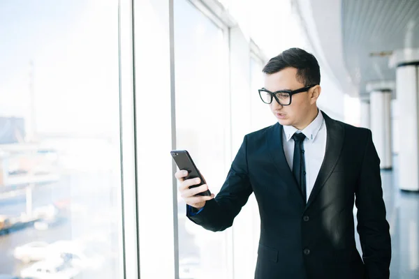 Pohledný podnikatel v obleku mobilní telefon umožňuje zkontrolovat e-mail nebo napsat zprávu v místnosti úřadu — Stock fotografie