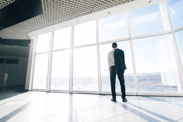 Jeune homme d'affaires détendu avec veste au-dessus des épaules dans les fenêtres panoramiques modernes du bureau — Photo