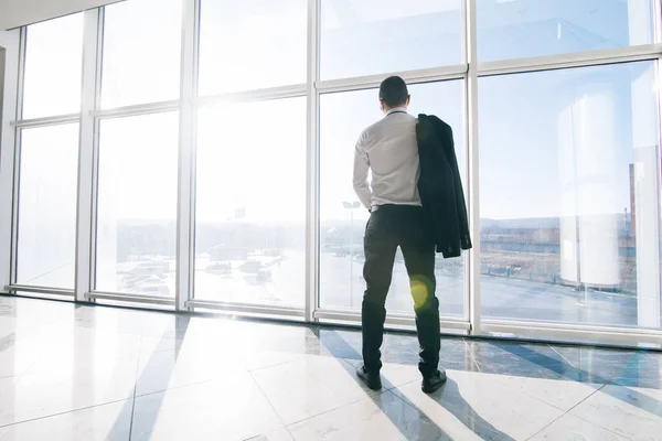 Jeune homme d'affaires détendu avec veste au-dessus des épaules dans les fenêtres panoramiques modernes du bureau — Photo