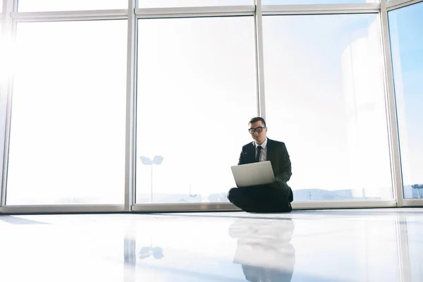 Бизнесмен на полу с ноутбуком в панорамных окнах — стоковое фото