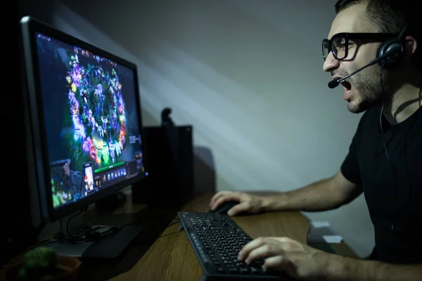 Молодой игрок в наушниках и очках с помощью консоли и компьютера для игры — стоковое фото