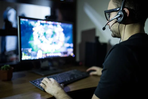 Joven jugador en auriculares y gafas usando la computadora para jugar en casa —  Fotos de Stock