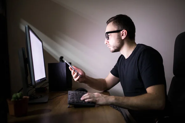 Человек пользуется телефоном рядом с компьютером — стоковое фото