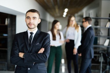 Arkadaşlarıyla modern ofis çapraz elleriyle önünde genç Yöneticisi.