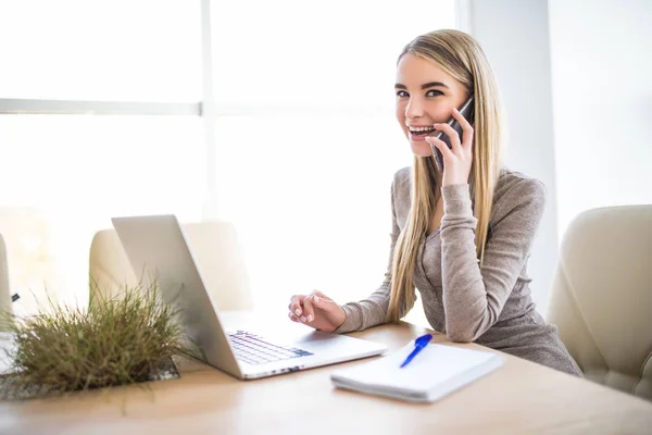 Egy fiatal üzleti nő portréja beszélni telefonon és használata laptop, iroda. Nézd meg kamera. — Stock Fotó
