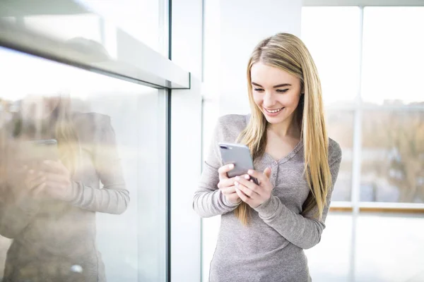 Portret van een jonge vrouw tekst bedrijfstelefoon tegen panoramische ramen — Stockfoto