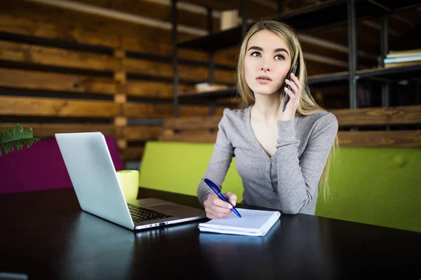 Fiatal üzleti nő a coworking beszélni a telefon, és észrevesz-ban jegyzetfüzet — Stock Fotó