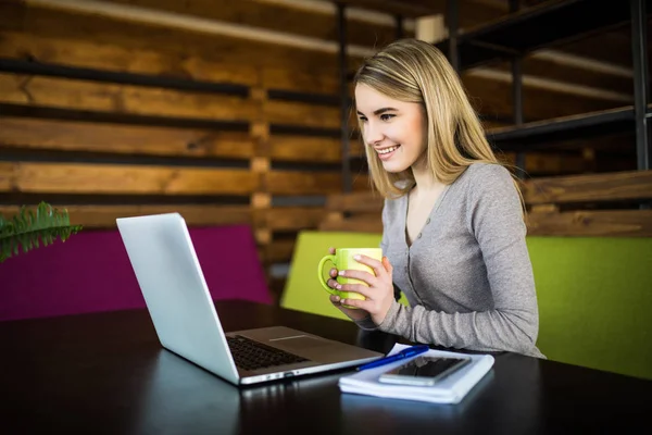 Jong meisje met kopje in handen kijken laptop op werkplek — Stockfoto