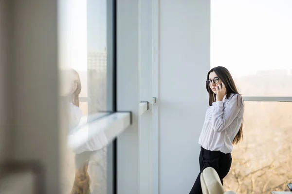 ビジネスの女性がスマートのモダンな空間で大きな事務所の窓の近くに電話で話す. — ストック写真