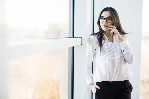 ビジネスの女性がスマートのモダンな空間で大きな事務所の窓の近くに電話で話す. — ストック写真