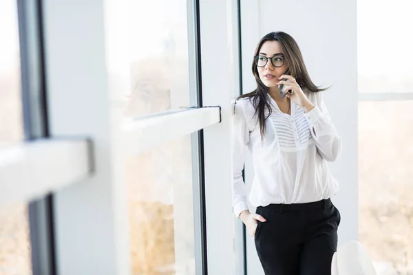 Business woman speak on phone near big office windows in modern smart space.